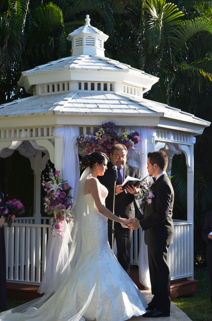 bride in wedding dress and groom in front of gazebo with flowers